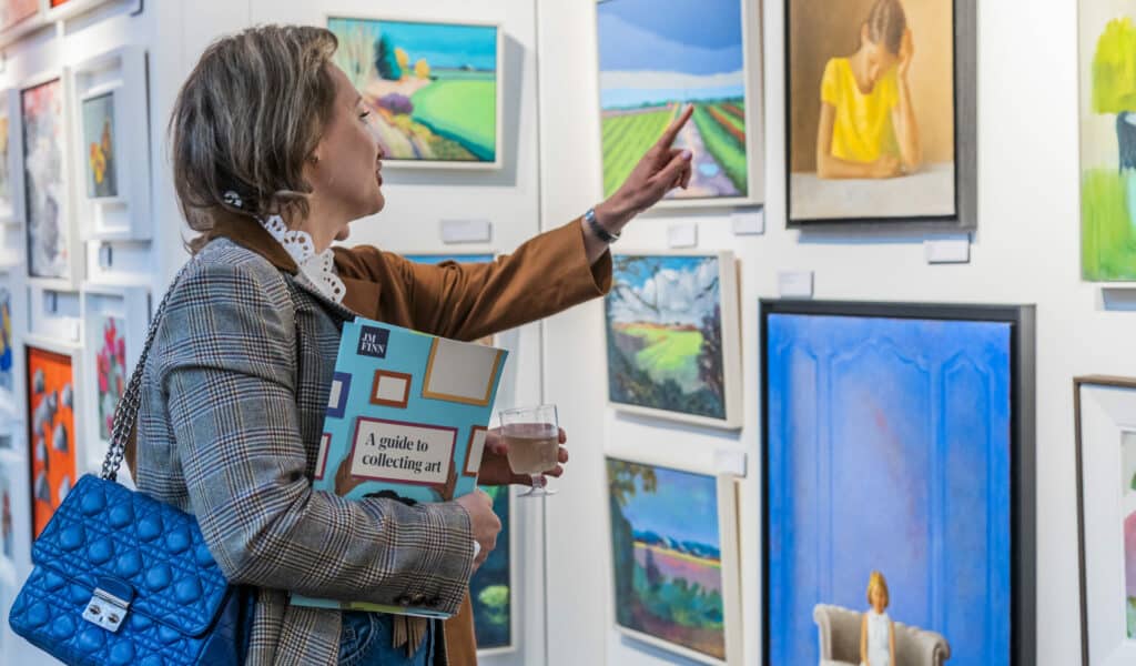 A photo of a woman pointing at an art piece at a Koestler Arts exhibition.
