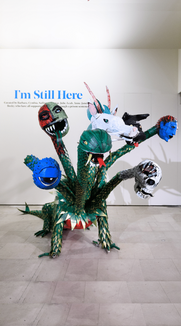 A photo of a large sculpture at a Koestler Arts exhibition, featuring a creature with multiple different types of heads.