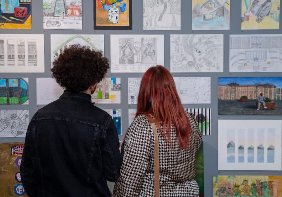 A photo of a couple stood in front of a wall filled with art.