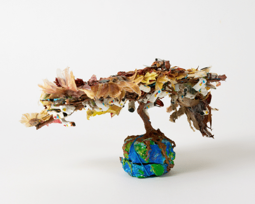 A papier-mache sculpture of a tree with roots growing on top of a tiny earth. The tree has CCTV cameras hidden inside the leaves that look like birds.