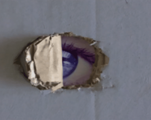 A film still of a piece of oval shaped cardboard peeled back to reveal a blue-coloured eye.