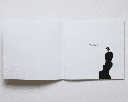 A white book with text reading, 'For Louis', next to a silhouette of a bird on top of a set of stones.
