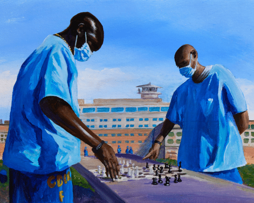 Two figures stood in prison outdoor space playing chess. They are wearing medical masks and prison-issue loose blue t-shirts.