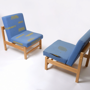 Two prison-issue blue fabric chairs facing each other with words and designs stitched into them.